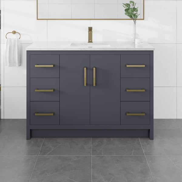 Curio 48″ Vanity in dark blue features gold handles and a sleek Carrara quartz top. This 48″ vanity includes a single sink, a towel hanging on the left side, and is complemented by a green plant and mirror above it on a tiled wall, with gray tiles covering the floor.