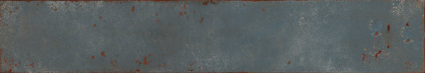 The Eclipse 2x18 Glazed Porcelain Tile features a rectangular shape and blue-gray surface with scattered reddish-brown accents, textured edges, and an industrial weathered look reminiscent of architectural metal.