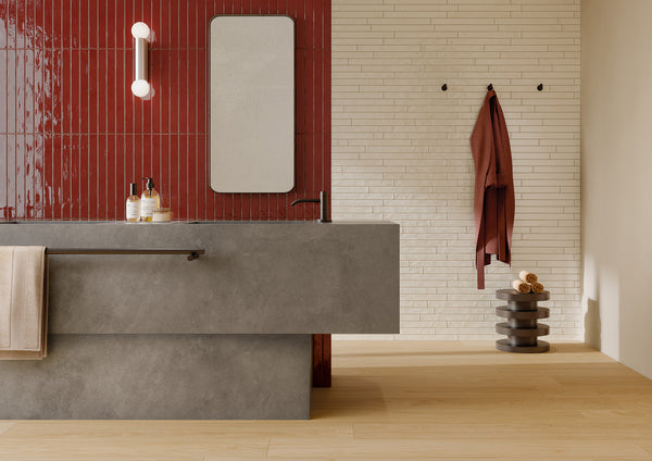 Modern bathroom with a gray concrete sink, red vertical tile wall, rectangular mirror, white wall sconce, beige towel, white brick accent wall, round hooks, brown hanging robe, and stacked dark shelves with rolled towels.