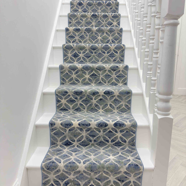 The Eclipse 63396-5666 Runner Rug in blue and white patterns adds a modern, stylish touch to a staircase with white steps and railings.