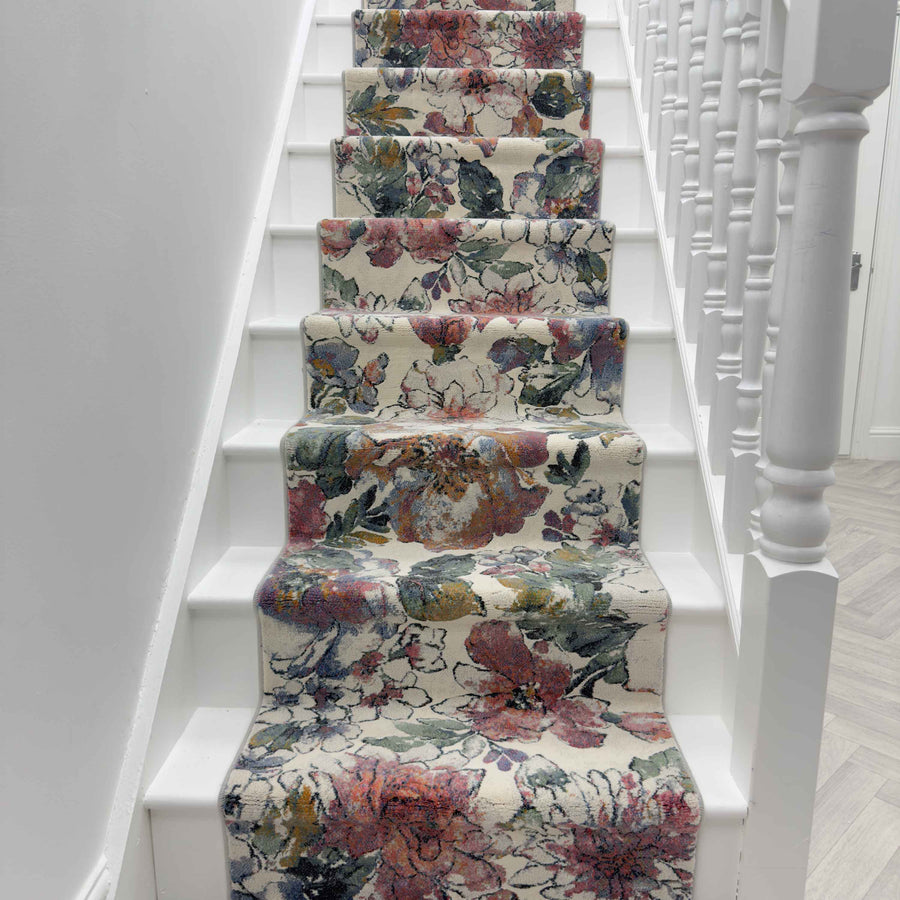A staircase with white steps and railing features the Eclipse 63528-6626 Runner Rug, showcasing a luxury floral pattern in pink, green, and orange. The view is from the base of the stairs looking upward.