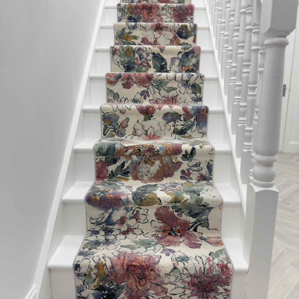 A staircase with white steps and railing features the Eclipse 63528-6626 Runner Rug, showcasing a luxury floral pattern in pink, green, and orange. The view is from the base of the stairs looking upward.