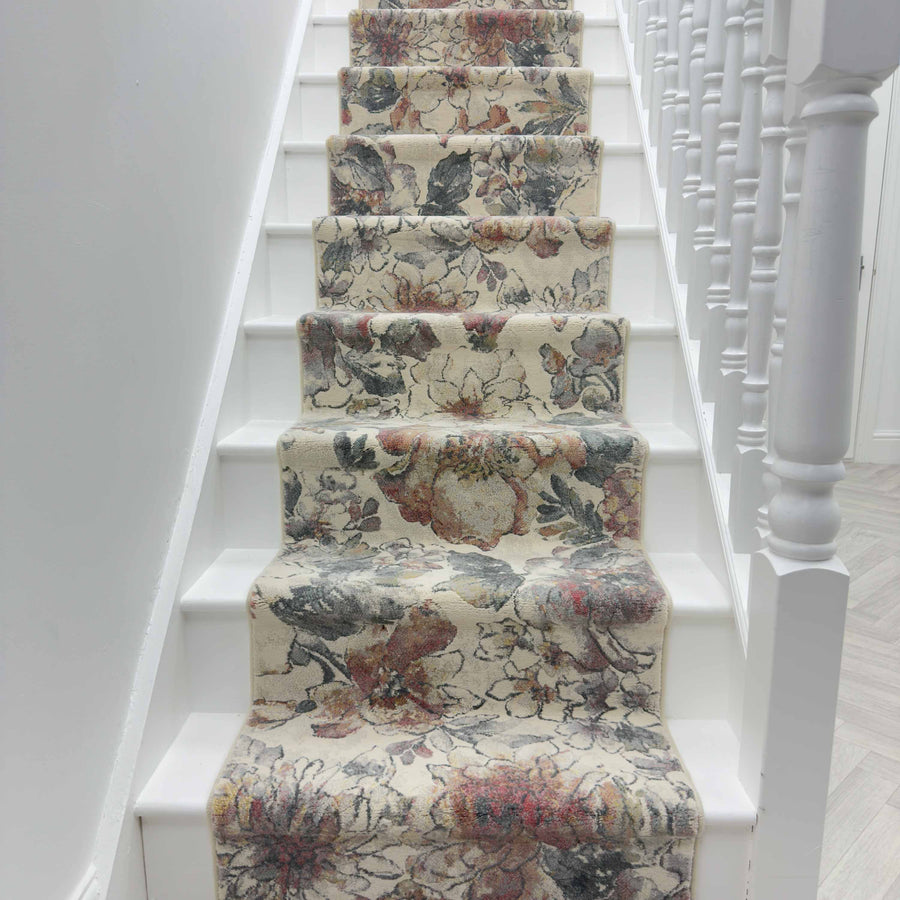 A staircase with white steps features the Eclipse 63528-6626 Runner Rug, showcasing a floral design in beige, gray, and muted red, bordered by white spindles and a handrail on the right side.