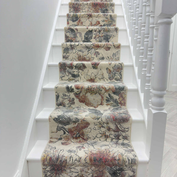 A staircase with white steps features the Eclipse 63528-6626 Runner Rug, showcasing a floral design in beige, gray, and muted red, bordered by white spindles and a handrail on the right side.