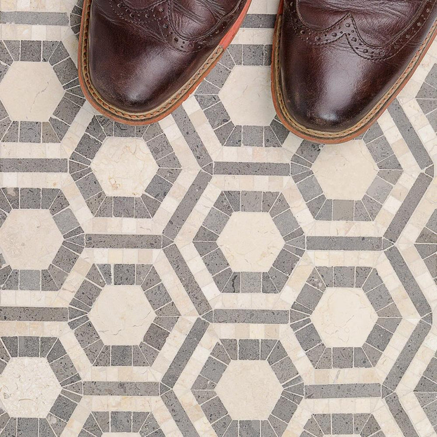 Close-up of brown leather dress shoes standing on hexagonal patterned floor tiles in shades of gray and beige, arranged in a geometric, mosaic design.