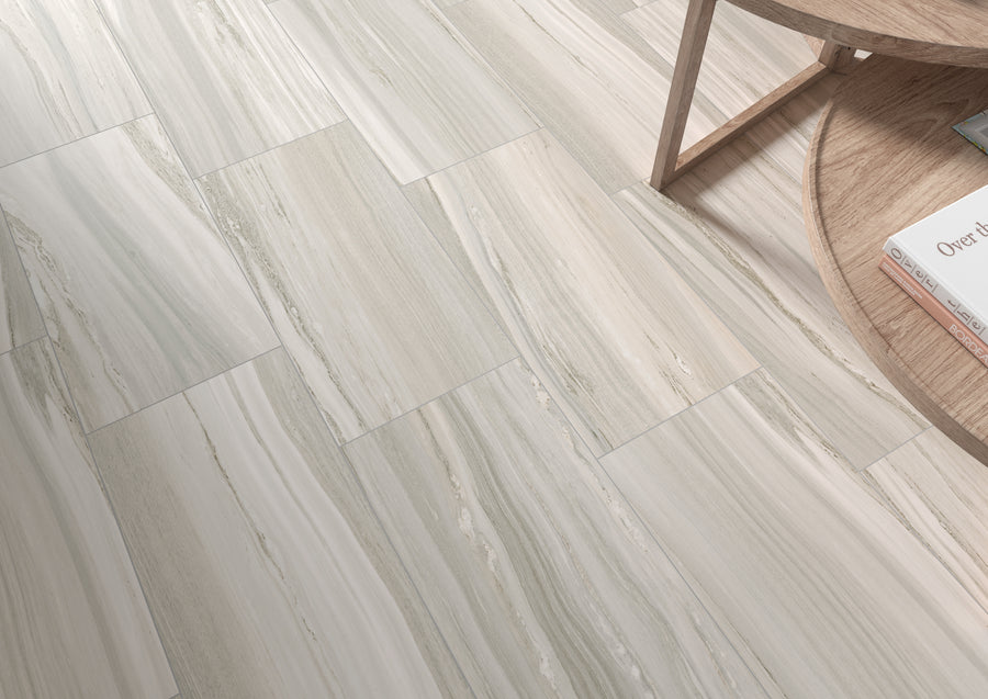 Light-colored rectangular tiles with subtle beige and gray veining form a clean, modern floor. In the corner, a wooden table with rounded edges holds a few books, adding a touch of warmth to the scene.