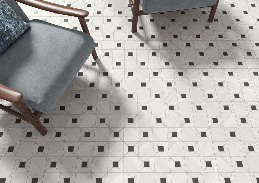 Two wooden chairs with gray cushions sit on a light-colored tile floor with a geometric pattern of octagons and small black squares at the corners. Shadows from the chairs fall across the patterned floor.