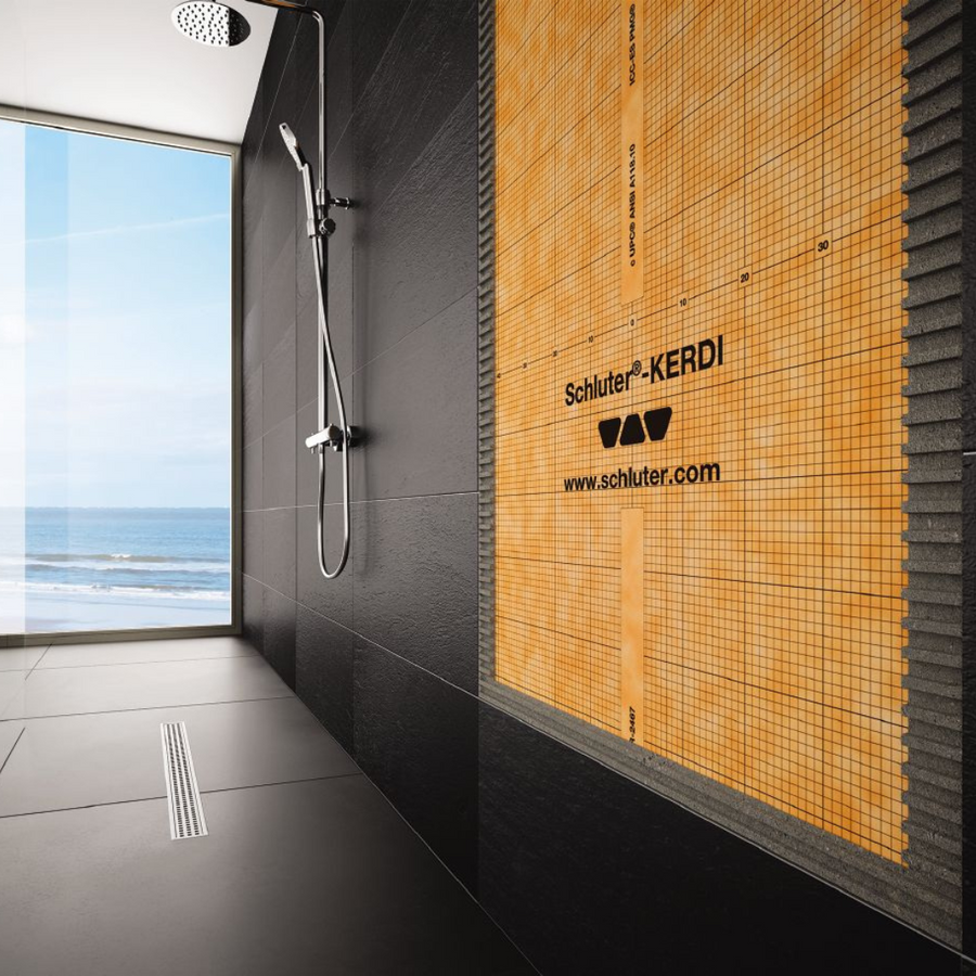 A modern black-tiled shower with a large window overlooks the sea. One wall features partially installed Schluter Kerdi Membrane, while a sleek showerhead is mounted above a linear floor drain.