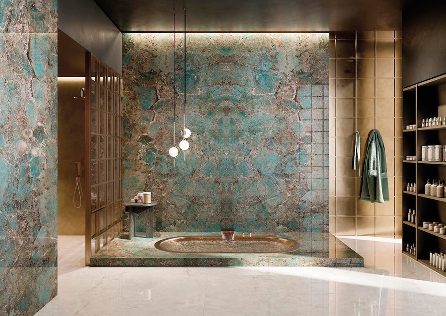 Luxurious bathroom featuring a large marble tub with turquoise and brown veining, matching wall, modern pendant lights, glass shower, gold tiles, shelves with toiletries, and green towels hanging on the wall.