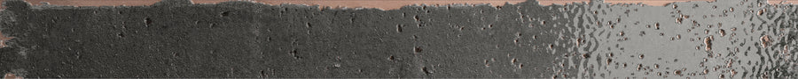 The Emerge 2x20 Porcelain Tile in Eclipse features a rough, dark-textured left side that fades into a smoother, lighter right, accented by vertical streaks and hints of copper in the background.
