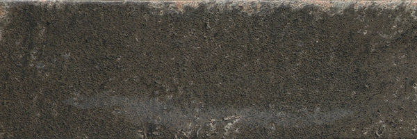 A close-up of Emerge 3x8 Porcelain Tile in Eclipse reveals a dark, weathered surface with natural variation, rough texture, softly worn edges, and subtle patches of lighter gray and brown accents.