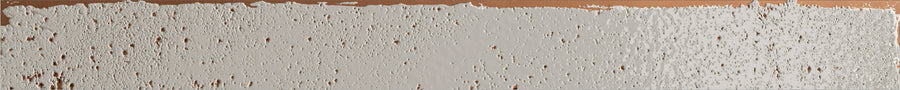 A flat Emerge 2x20 Porcelain Tile in First Light color is partially covered with white residue, featuring numerous small holes and irregular edges, exposing the glossy surface beneath.