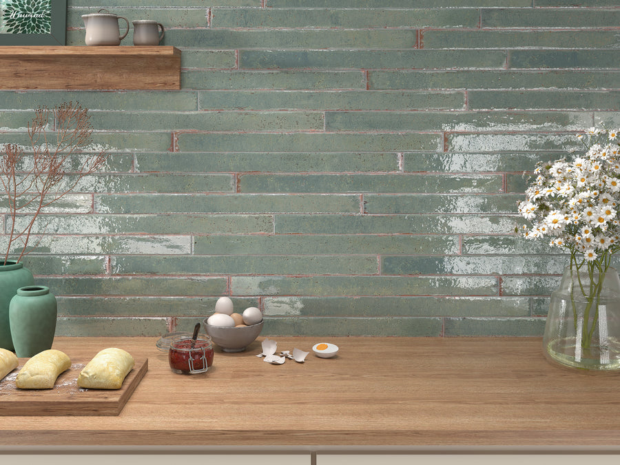 A kitchen countertop with dough, eggs, a jar of jam, and broken eggshells. Behind, glossy green tiles cover the wall, and shelves hold ceramic dishes and a vase. Fresh daisies sit in a jar on the right.