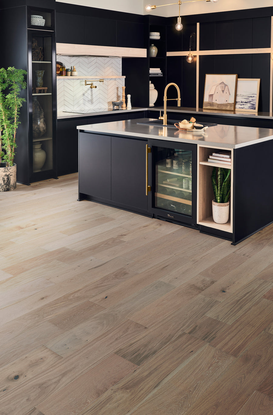 Modern kitchen with light wood flooring, dark cabinets, a central island with a built-in wine fridge, open shelving with decor and plants, and elegant pendant lighting.