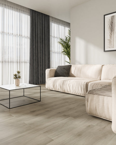 A modern living room with light wood flooring, a beige sofa, a black and white coffee table, a potted plant, dark curtains, and large windows with sheer white drapes letting in natural light.