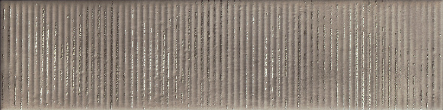 Close-up of the Urban Glow 4" x 16" Deco Subway Tile in Pewter, featuring vertical ridges and small holes. Its weathered brown-gray surface is highlighted by scattered bright spots shining through the openings.