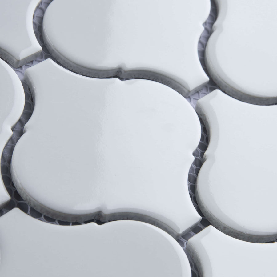Close-up of white, glossy, arabesque-shaped ceramic tiles with dark grout lines in between, showing a repeating geometric pattern and slight texture on the tile surfaces.