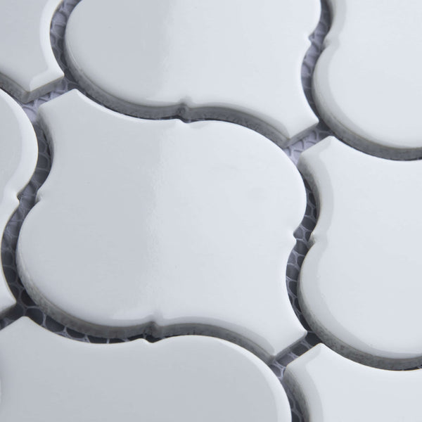 Close-up of white, glossy, arabesque-shaped ceramic tiles with dark grout lines in between, showing a repeating geometric pattern and slight texture on the tile surfaces.