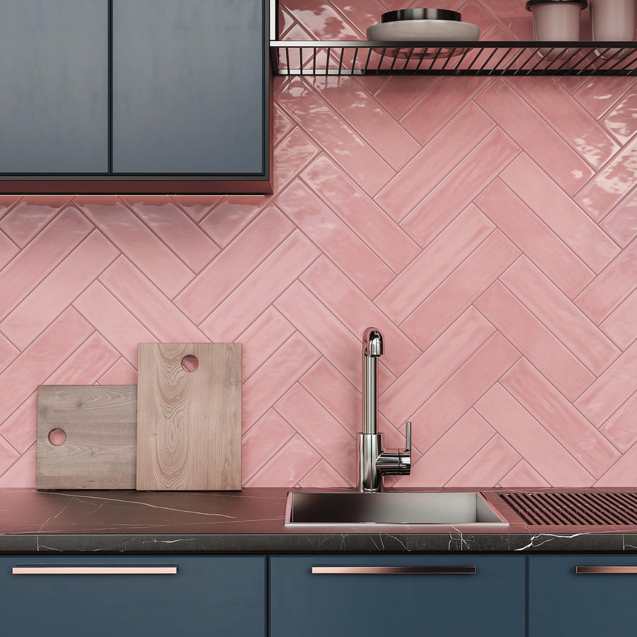A modern kitchen with dark blue cabinets, a black countertop, a stainless steel sink, wooden cutting boards, and a pink herringbone-patterned tile backsplash.