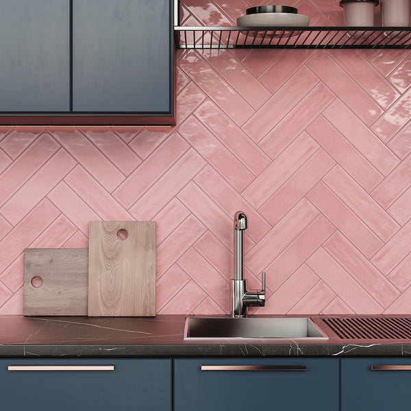 A modern kitchen with dark blue cabinets, a black countertop, a stainless steel sink, wooden cutting boards, and a pink herringbone-patterned tile backsplash.