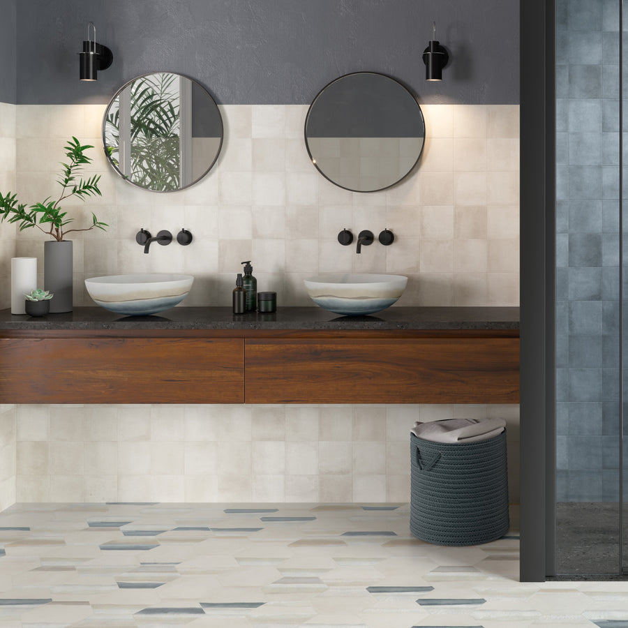 Modern bathroom with double sinks on a wooden vanity, two round mirrors, wall-mounted faucets, black fixtures, decorative plants, and a woven laundry basket on a patterned tile floor.