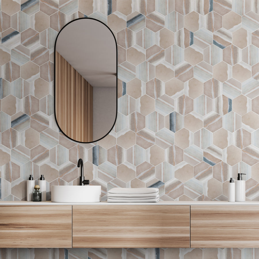 Modern bathroom with a wooden vanity, oval mirror, round white sink, black faucet, and geometric hexagon-patterned tile wall in neutral tones. Stacked white towels and soap dispensers sit on the countertop.