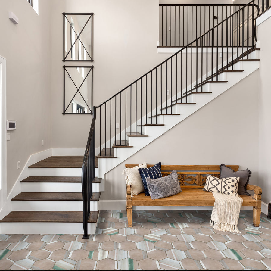 A modern entryway features a wooden bench with pillows and a blanket, geometric tile flooring, a white staircase with dark railings, and two wall mirrors. Neutral tones and clean lines create a welcoming atmosphere.