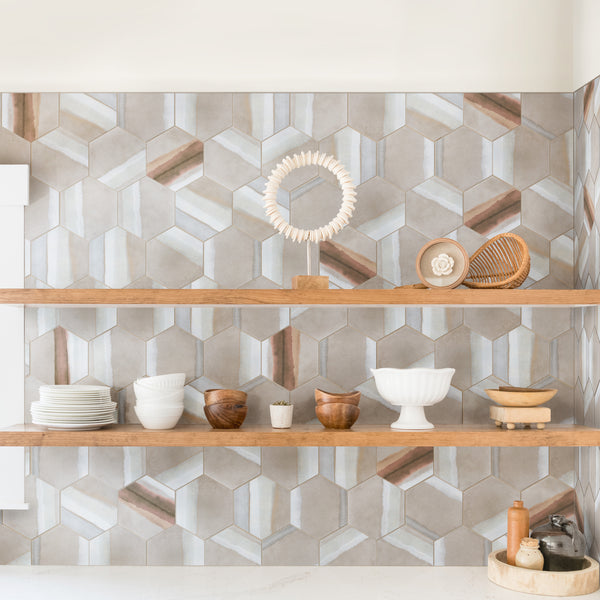 Open wooden shelves against a geometric hexagon-patterned backsplash, displaying dishes, bowls, a plant, wooden decor, ceramics, and kitchen items in neutral and earthy tones.