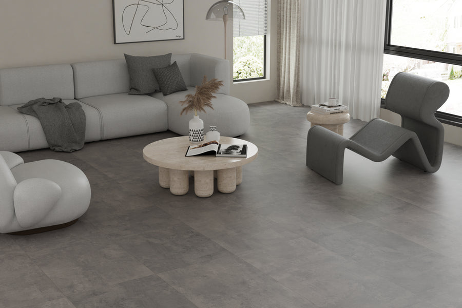 Minimalist living room with modern gray furniture, abstract wall art, a round stone coffee table with decor, large windows with sheer curtains, and neutral tones throughout.