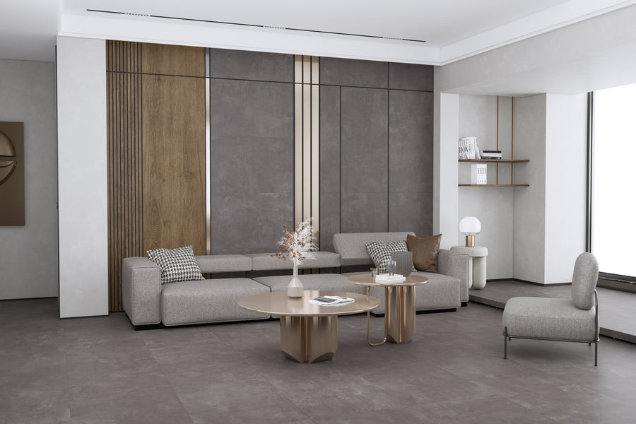 A modern living room with a gray sectional sofa, patterned cushions, a gray accent chair, two round coffee tables, wall paneling in wood and gray tones, and minimal decorative items on shelves and tables.