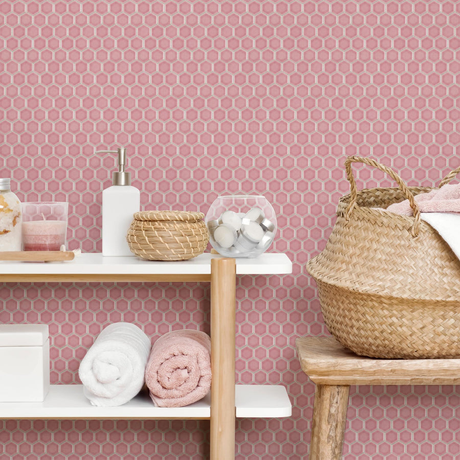 A bathroom with pink hexagonal tile walls, white shelves holding towels, soap, and jars, and a woven basket with towels on a wooden stool. The decor is neat and organized.