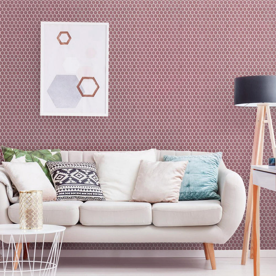 A modern living room with a white sofa, assorted patterned pillows, a round white coffee table, a black floor lamp, and light pink hexagon-patterned wallpaper with framed wall art above the couch.
