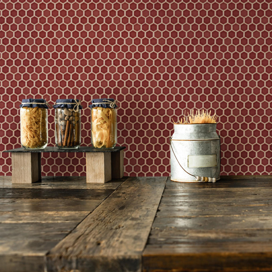 Three jars filled with dried foods sit on a wooden shelf, next to a metal container holding wooden sticks, all placed on a rustic wooden table with a red hexagonal tile wall in the background.