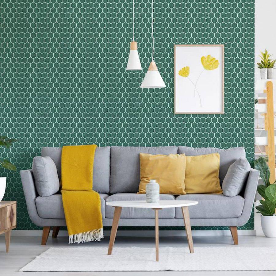 A modern living room with a light gray sofa, yellow pillows, and a yellow throw. A white coffee table sits in front. The green hexagonal tile wall has a yellow flower artwork, and pendant lights hang above. Plants and decor add accents.