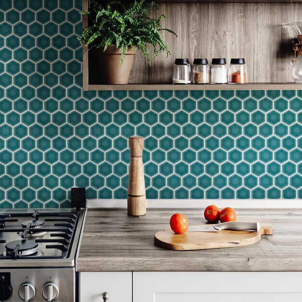 A modern kitchen features a teal hexagon tile backsplash, wooden countertop with tomatoes on a cutting board, a pepper mill, gas stove, and open shelf with spice jars and a potted plant.