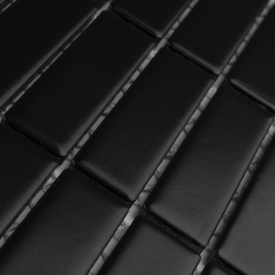Close-up of black rectangular tiles arranged in a staggered, brick-like pattern with faint gray grout lines visible between them. The tiles have a smooth, matte finish.
