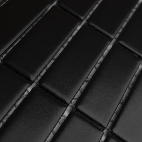 Close-up of black rectangular tiles arranged in a staggered, brick-like pattern with faint gray grout lines visible between them. The tiles have a smooth, matte finish.