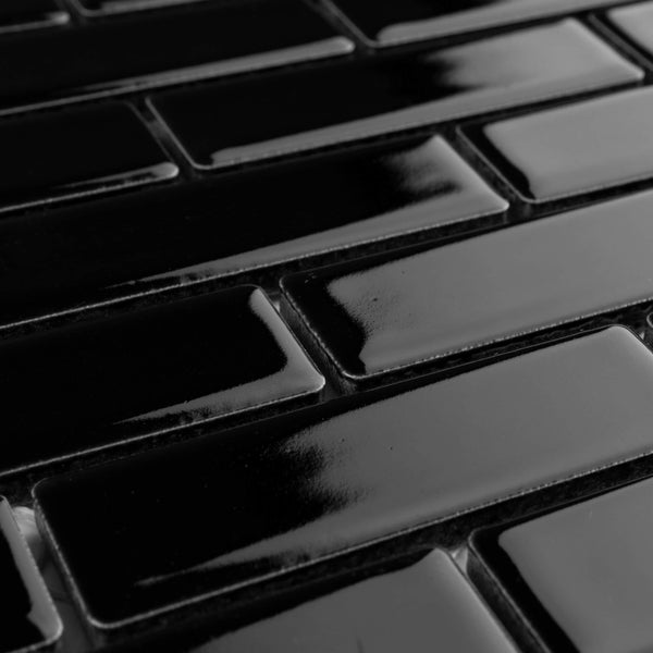Close-up view of glossy black rectangular tiles arranged in a staggered brick pattern. The tiles have a smooth, reflective surface with subtle highlights and shadows.