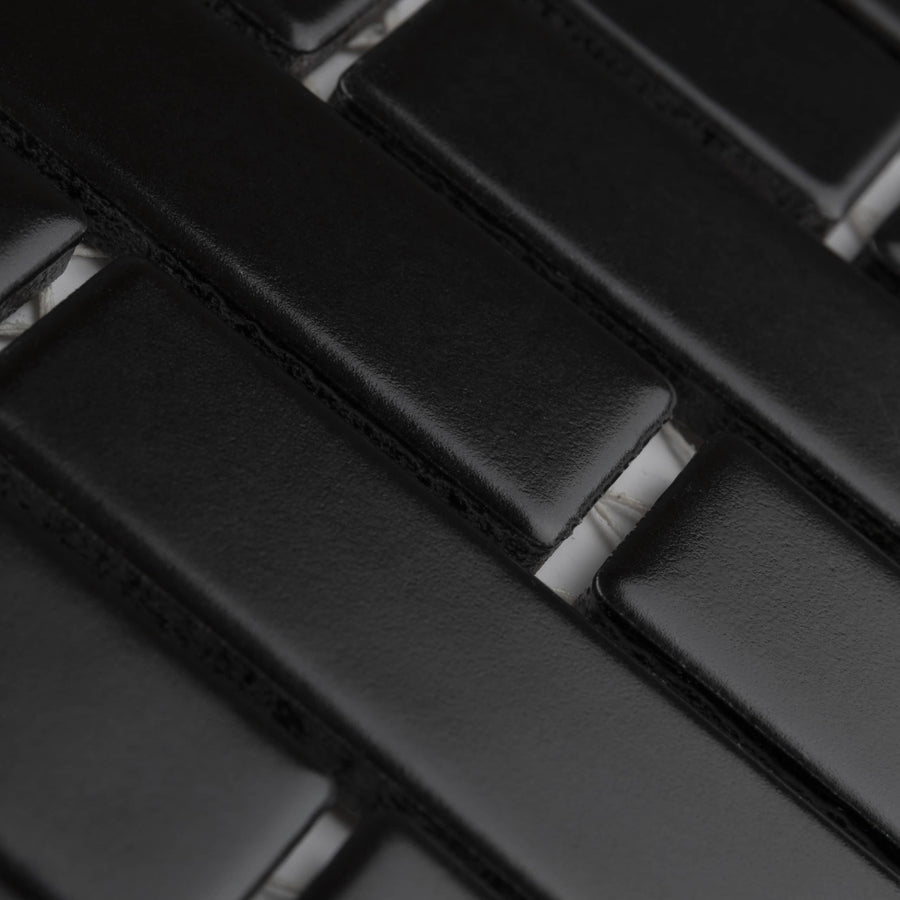 Close-up of a black rectangular tile mosaic with a glossy finish, arranged in a staggered brick pattern. The grout lines between the tiles are visible, highlighting the geometric design.