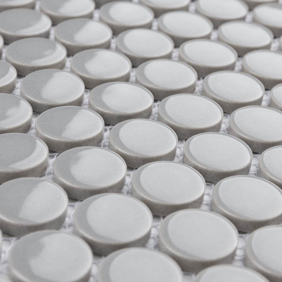Close-up of a tiled surface featuring smooth, glossy, round gray tiles arranged in a grid pattern on a mesh backing. The tiles have a slightly raised appearance and reflect light.