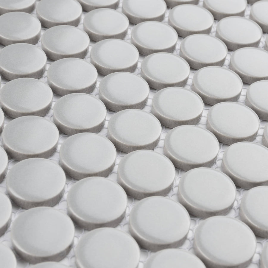 Close-up view of a surface with a repeating pattern of round, light gray tiles arranged in a grid on a white background.