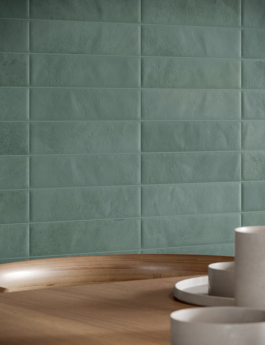 Matte teal rectangular tiles arranged in a horizontal grid on a wall, with a wooden surface and several white cylindrical objects placed in the foreground.
