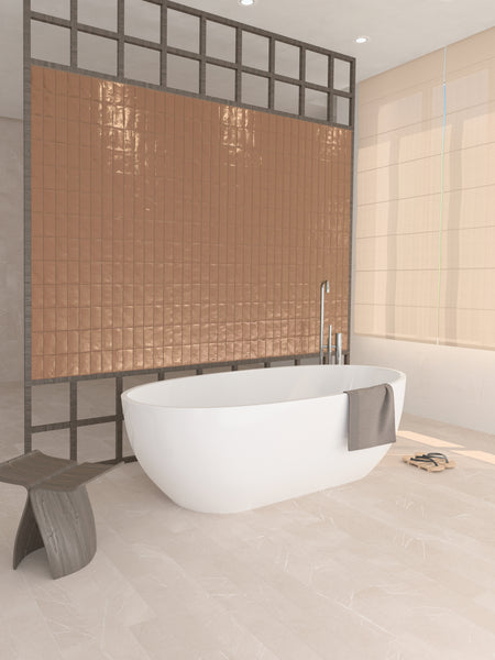 A modern bathroom with a white freestanding bathtub, a gray towel draped on the edge, a small wooden stool, beige tiled floor, and a copper-colored tiled accent wall behind the tub.