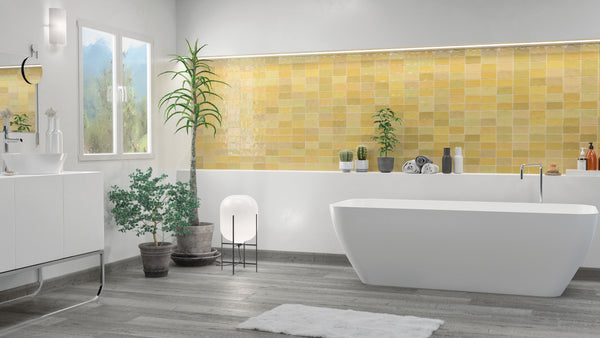 Modern bathroom with a white bathtub, yellow-tiled accent wall, potted plants, a white vanity, grey wood flooring, and a floor lamp, creating a bright and refreshing atmosphere.