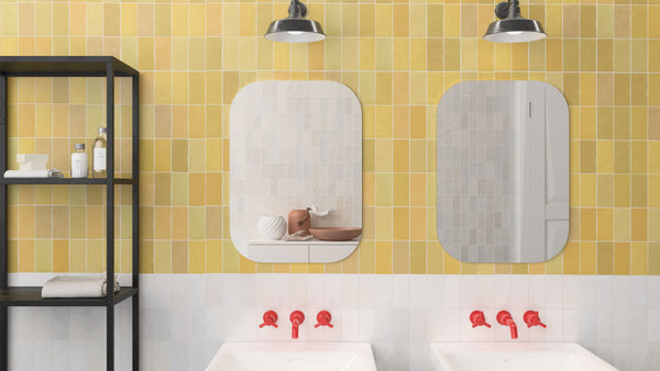 A bathroom with yellow and white tiled walls, two mirrors above double sinks with red faucets, black shelving on the left holding towels and toiletries, and two black industrial lights above the mirrors.