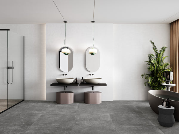 Modern bathroom with dual sinks, oval mirrors, hanging lights, large gray tile floor, a glass shower, a freestanding bathtub, a green potted plant, and neutral decor for a minimalist, elegant look.