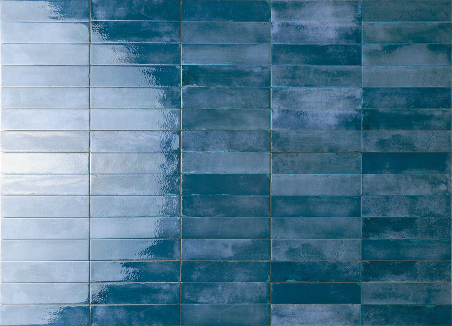 A wall of rectangular blue tiles with a gradient effect, transitioning from lighter, glossy tiles on the left to darker, matte tiles on the right.