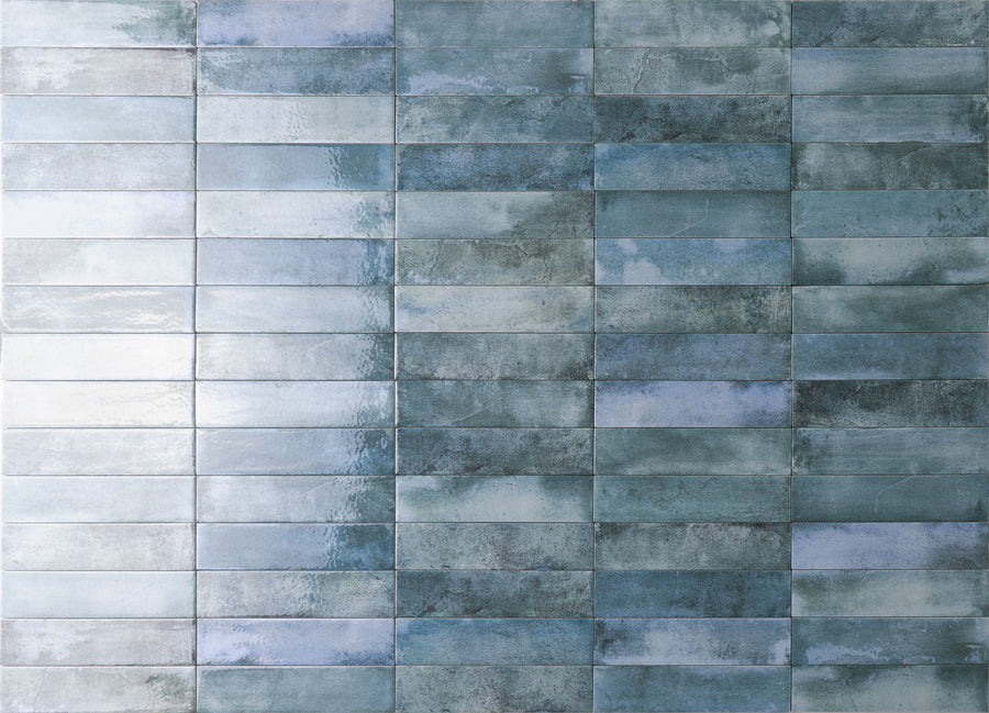 A wall covered with rectangular, glossy blue and gray tiles arranged in a horizontal grid pattern, creating a textured and slightly reflective surface.