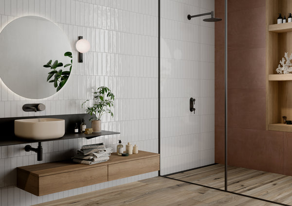 Modern bathroom with a floating wooden vanity, round mirror, wall sconce, potted plant, open shelving, and a glass-enclosed shower featuring minimalist fixtures. White tile and wood accents create a clean, contemporary look.