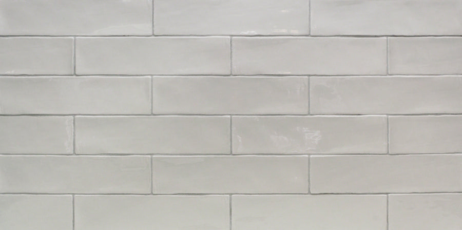A close-up of a wall with Masia 3" x 12" Subway Tile in Gris Claro, featuring glossy, rectangular tiles in a staggered brick pattern—perfect for accent walls or kitchen backsplashes.